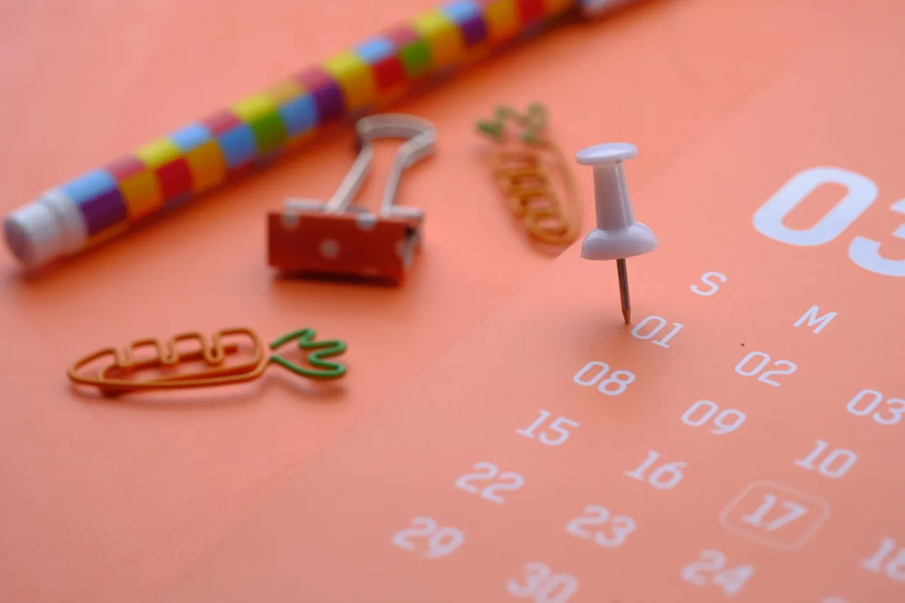 A push pin marking a date on an orange paper calendar.