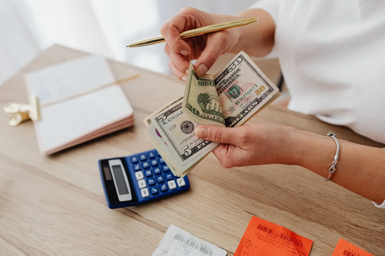 Woman counting cash with a calculator at a desk while managing her finances.