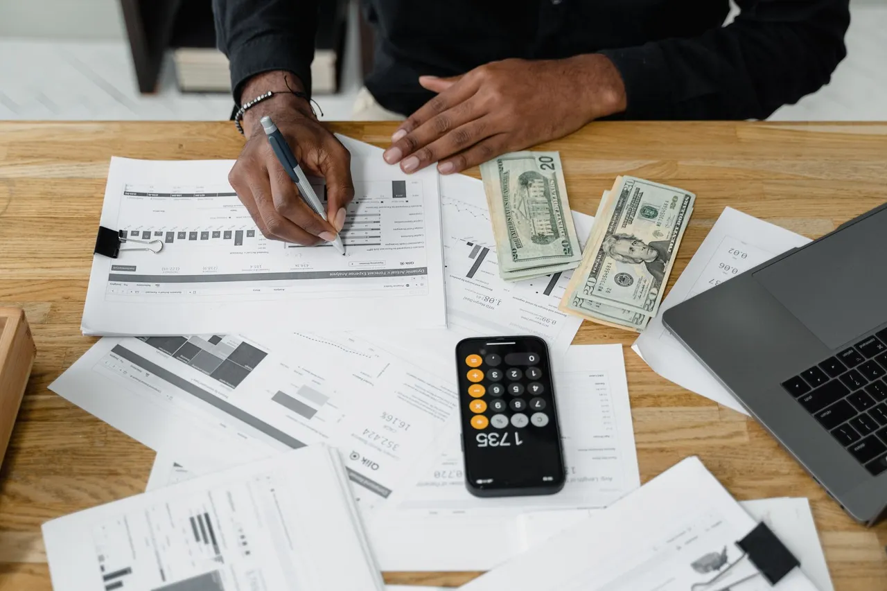 Man working on financial reports with a calculator, cash, and a laptop on a desk.