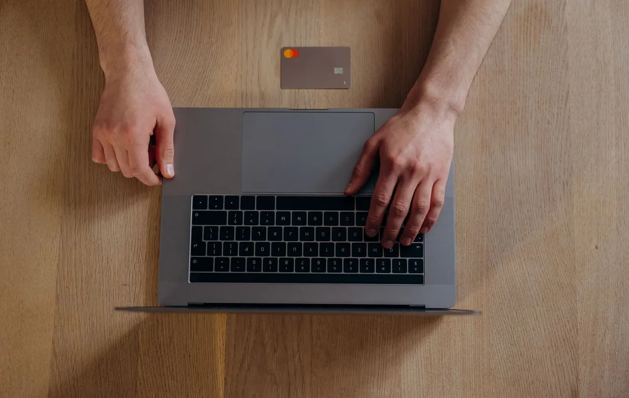 Top view of male hands on a laptop with credit card on wooden table, ideal for online shopping themes.