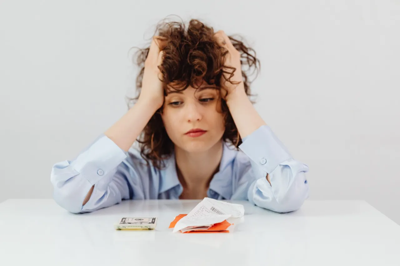 A woman looks stressed while sorting receipts and cash on a table.