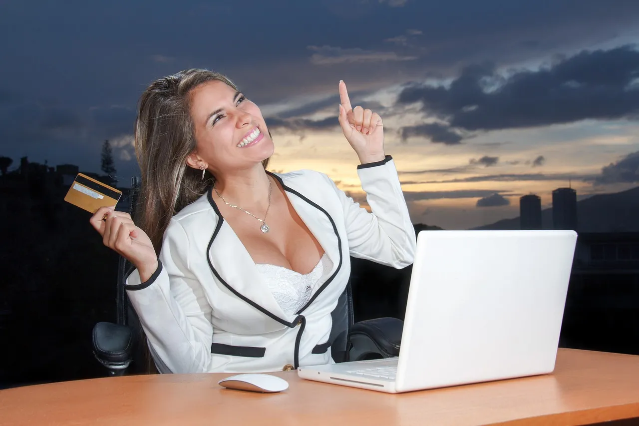 Woman in floral dress shopping online with a laptop and credit card indoors.