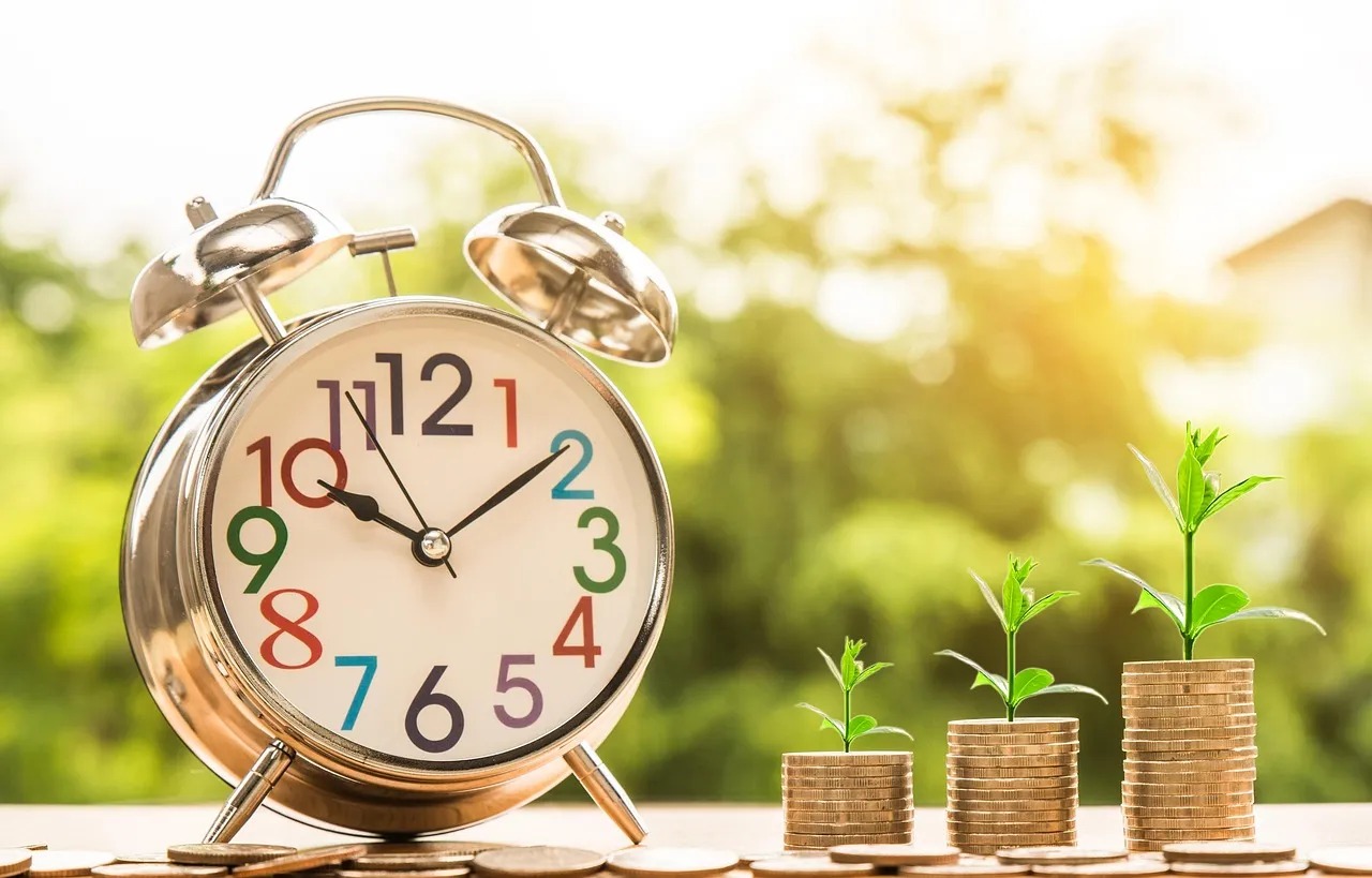 A clock beside a stack of coins and a small growing plant, suggesting savings growing over time.