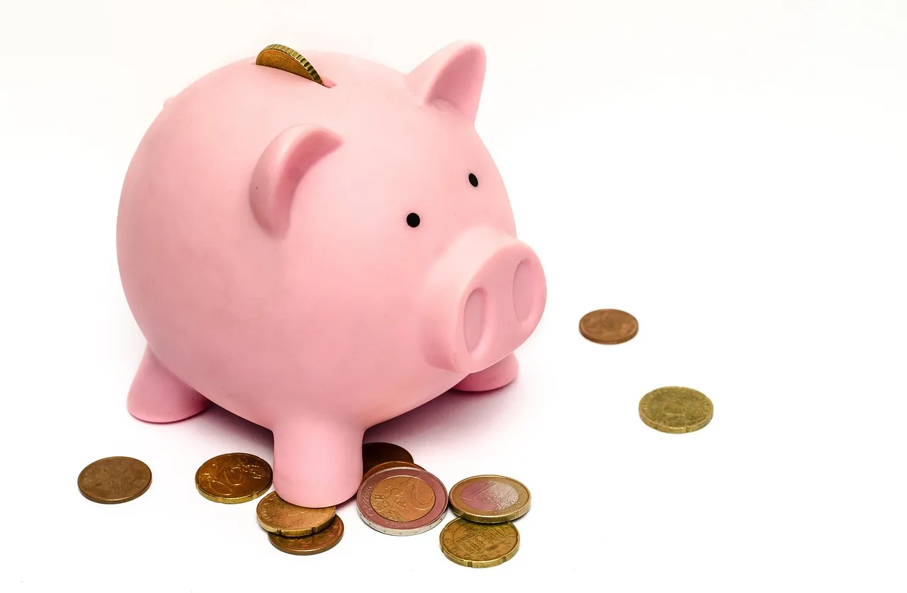 A piggy bank sitting beside a pile of coins.